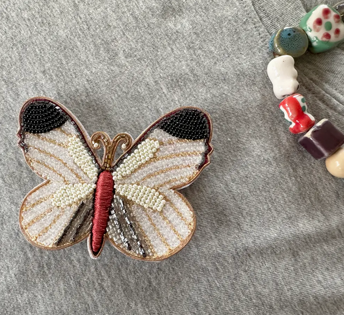 white butterfly beaded brooch pinned to gre tee-shirt