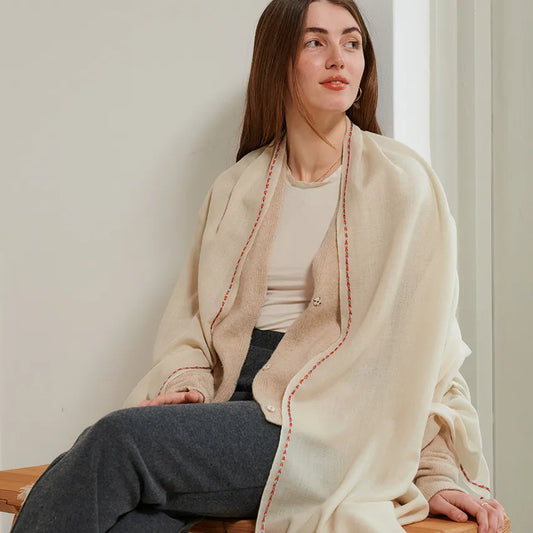 Dust color scarf with embroidery border stitch in orange and sky blue. Worn over a cream tee and open taupe cardigan. Model sitting with charcoal sweatpants