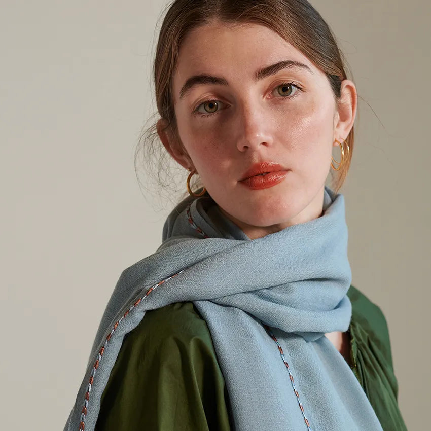 Sky color scarf with brown and sky stitch along border worn crossed over model's right shoulder over a green blouse