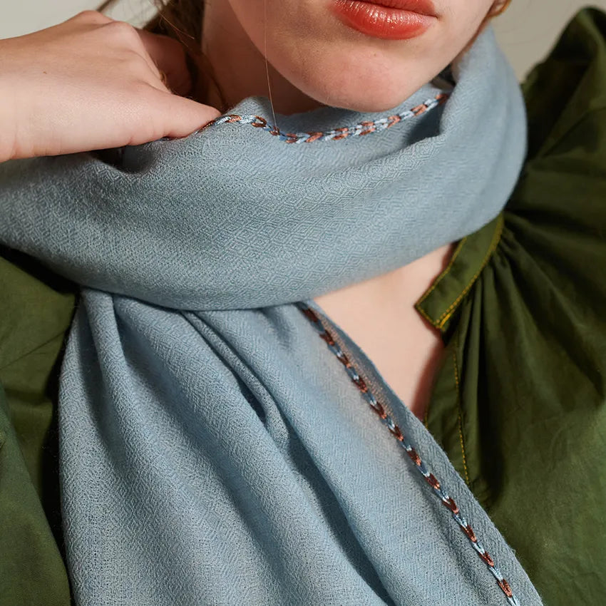 Detail of sky scarf with sky and brown border stitch worn over a green blouse