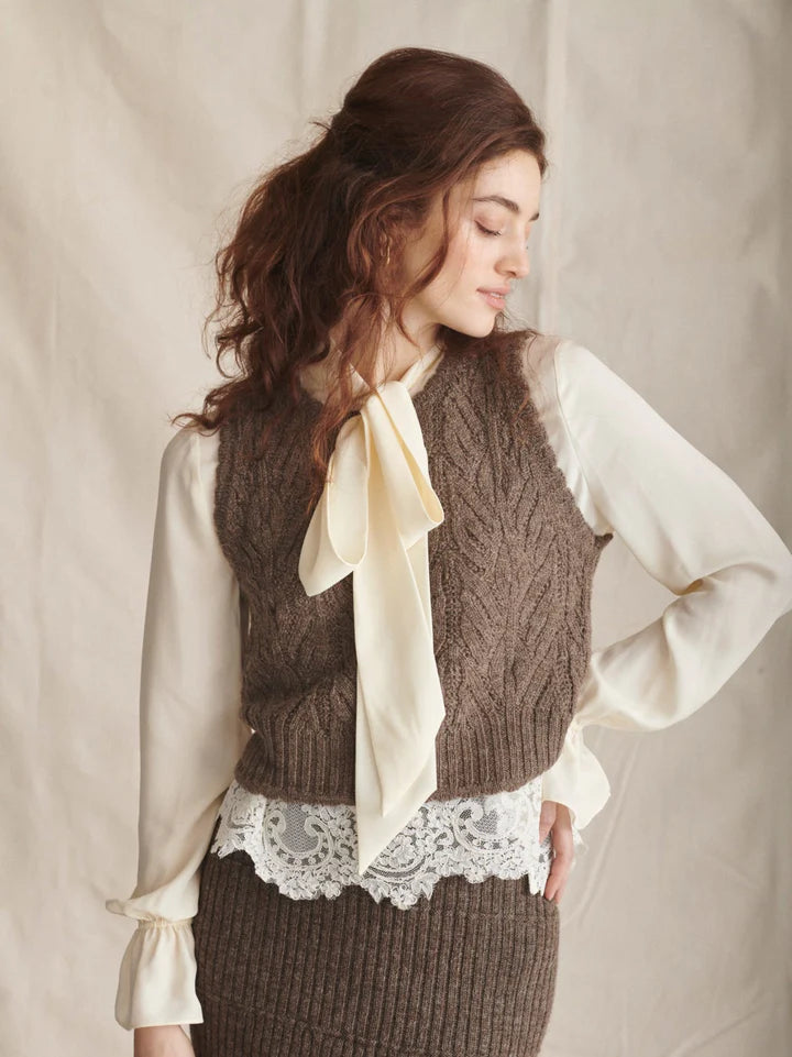 Woman wearing a brown knitted vest over a white blouse with a beige background
