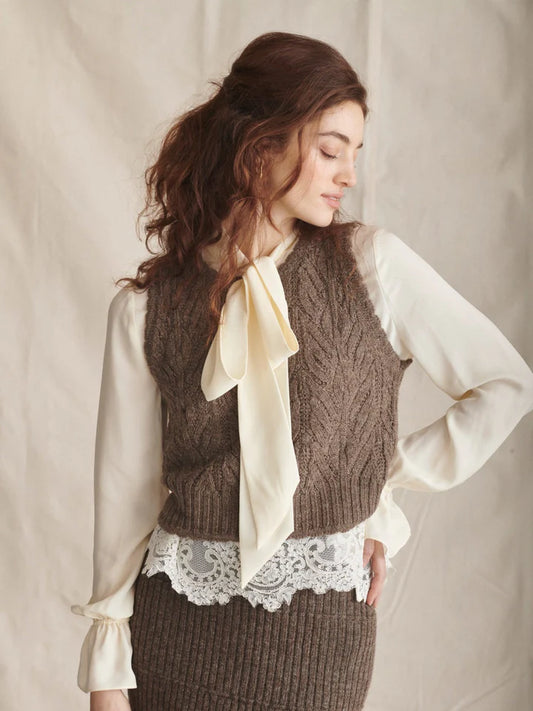 Woman wearing a brown knitted vest over a white blouse with a beige background