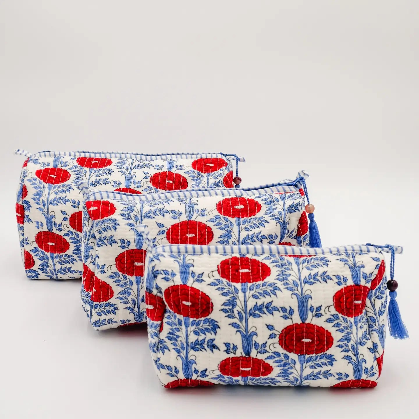 Three quilted fabric pouches with a blue floral and red medallion pattern, arranged diagonally on a light gray background.