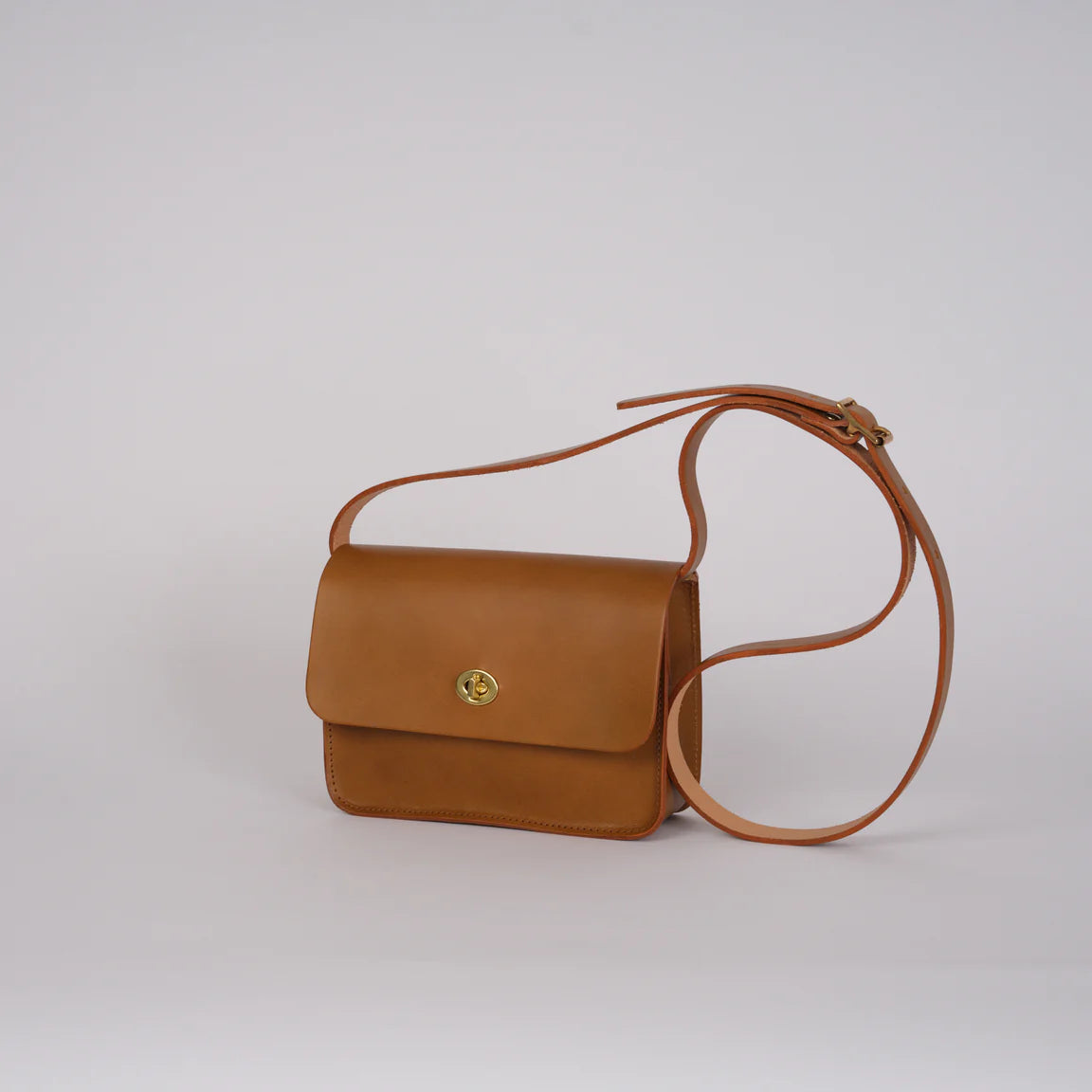 Brown leather handbag with a strap on a light gray background