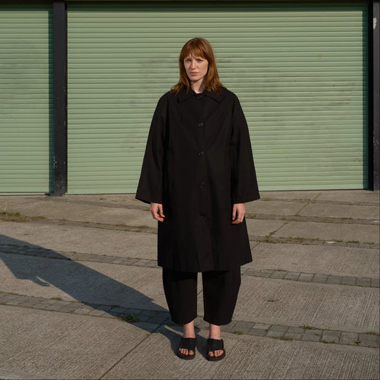 Person wearing a black coat standing in front of a green shutter.