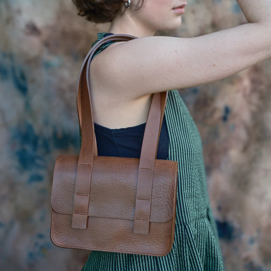 Woman holding a brown leather handbag with a blurred background