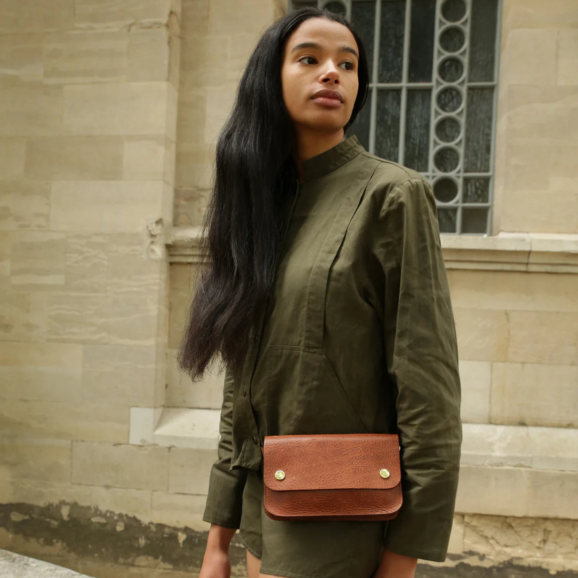 Woman wearing a green outfit with a brown leather bag in front of a stone building.