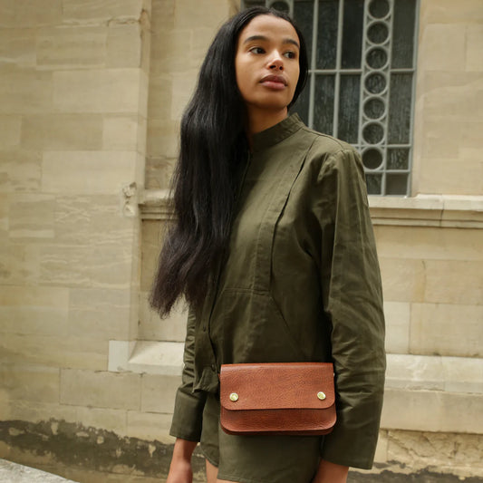 Woman wearing a green outfit with a brown leather bag in front of a stone building.