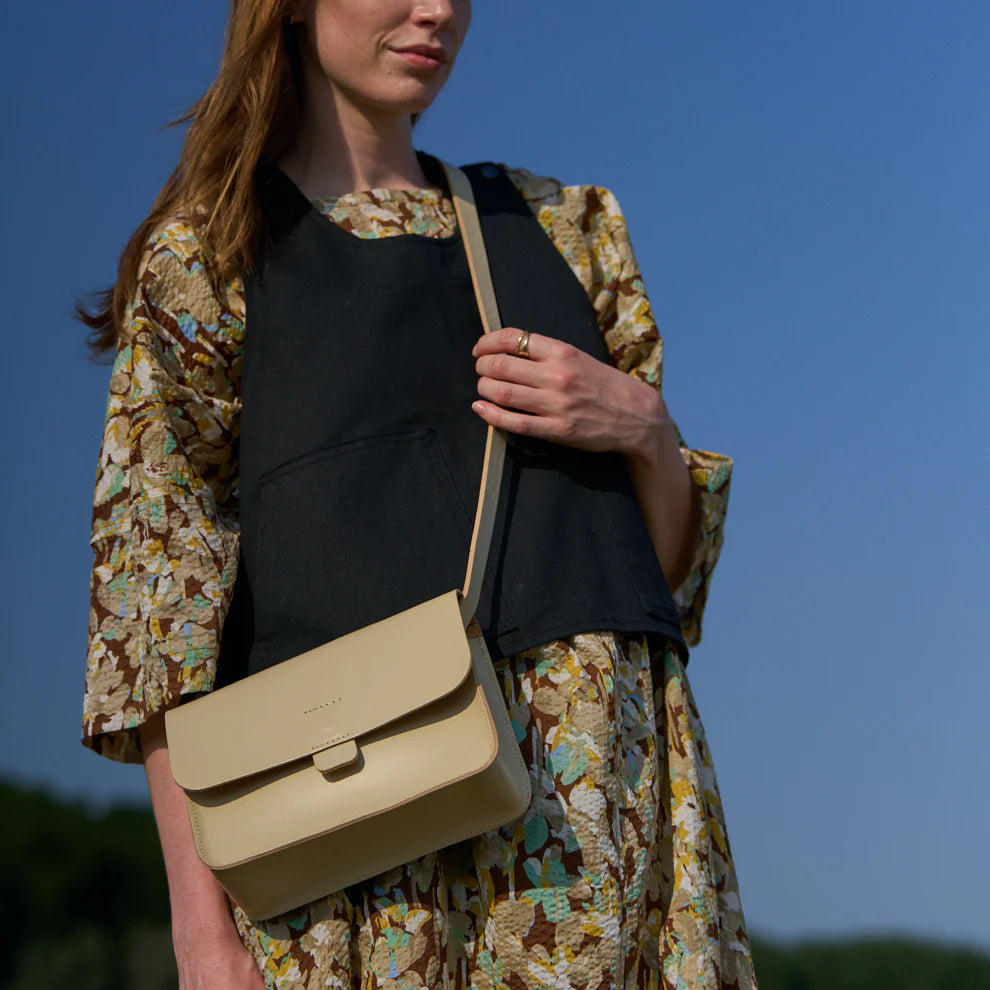 Woman holding a beige crossbody bag against a clear blue sky