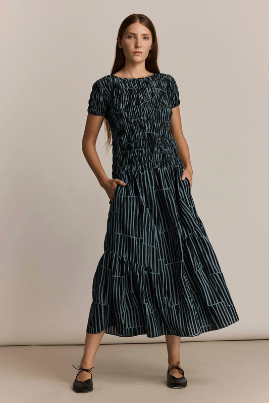 Woman wearing a black and green patterned skirt and top against a beige background