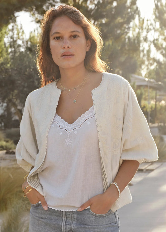 Woman wearing a light-colored cardigan over a white blouse with a blurred natural background