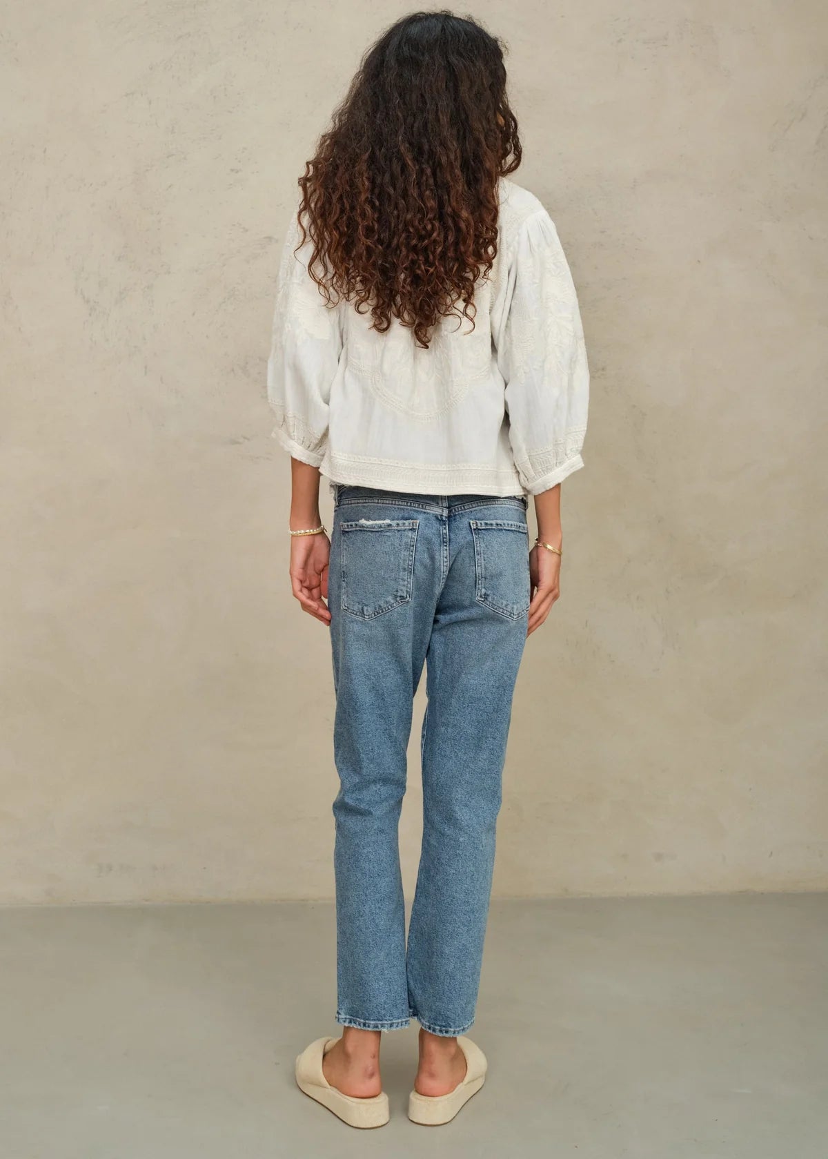 Person wearing a white blouse and blue jeans against a beige background