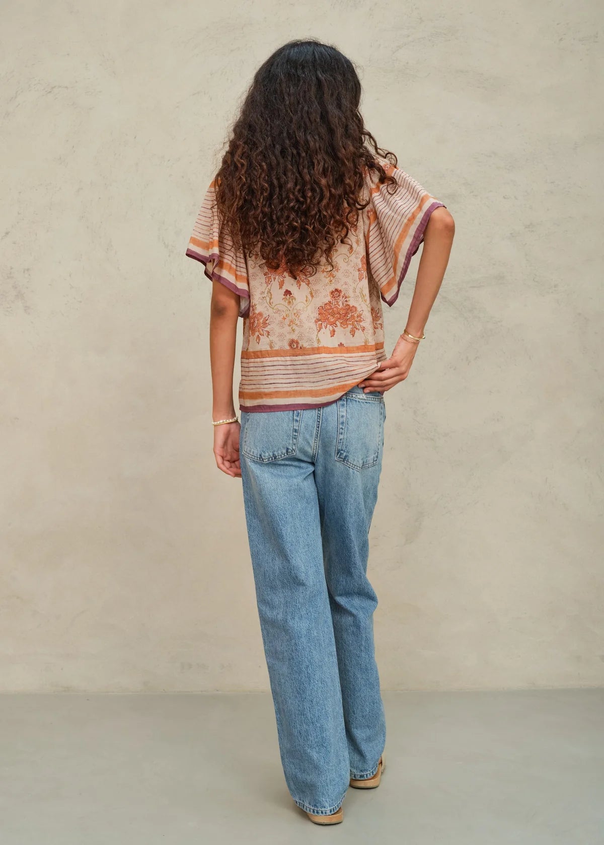 Person wearing a patterned top and blue jeans against a beige background