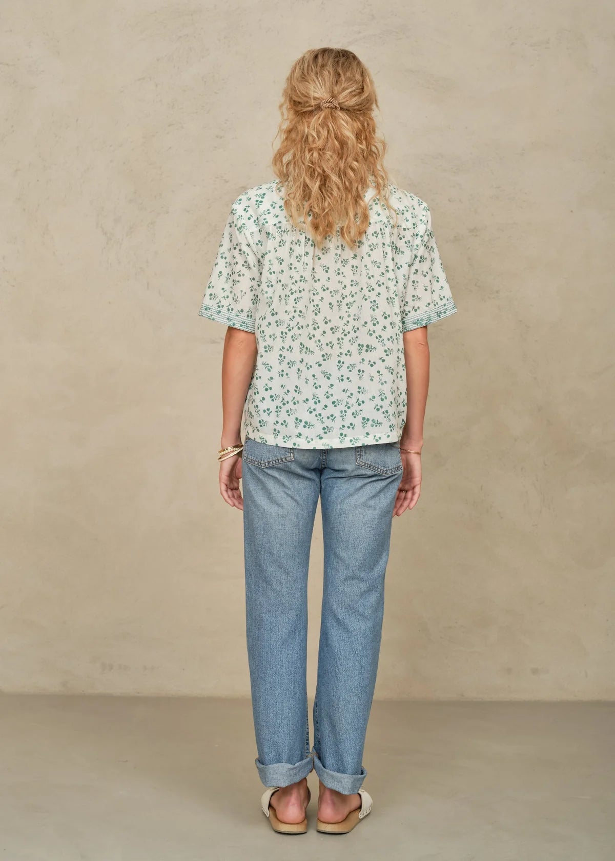 Person wearing a floral blouse and blue jeans against a beige background