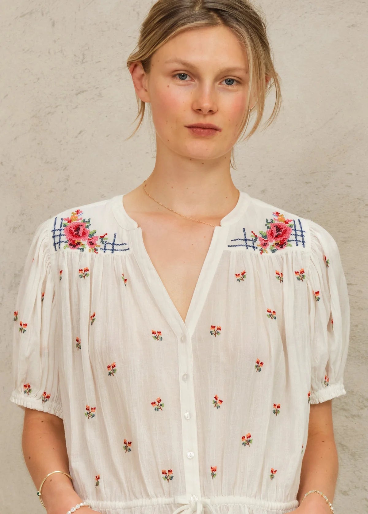 Woman wearing a white blouse with floral embroidery against a beige background