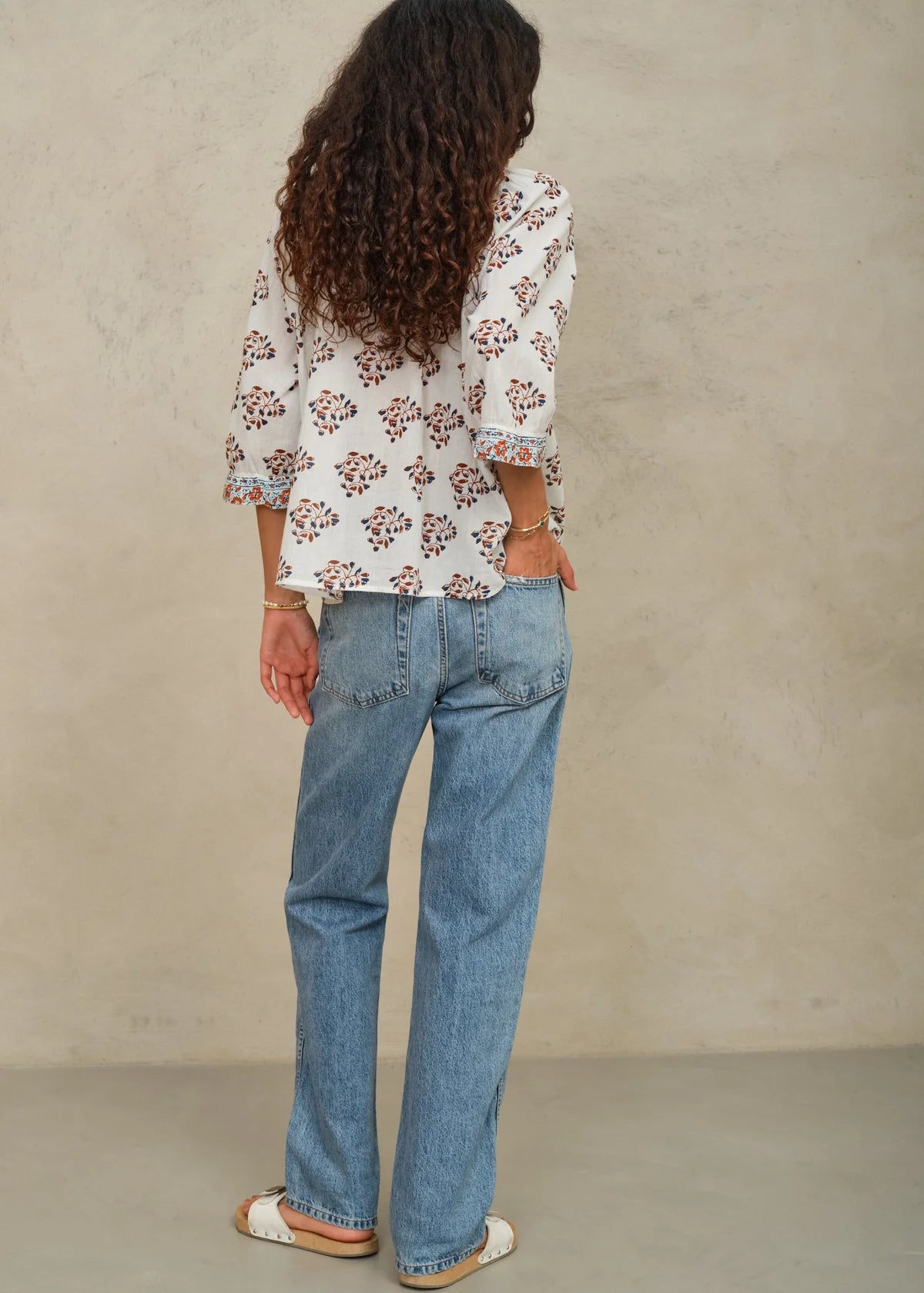 Person wearing a floral blouse and blue jeans against a beige background