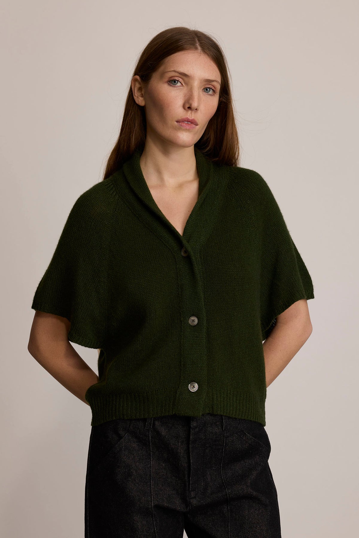 A model wears a forest green buttoned cardigan with short sleeves and black denim pants.
