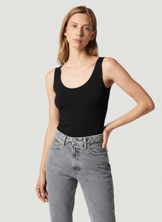 Woman wearing a black tank top and gray jeans against a light gray background