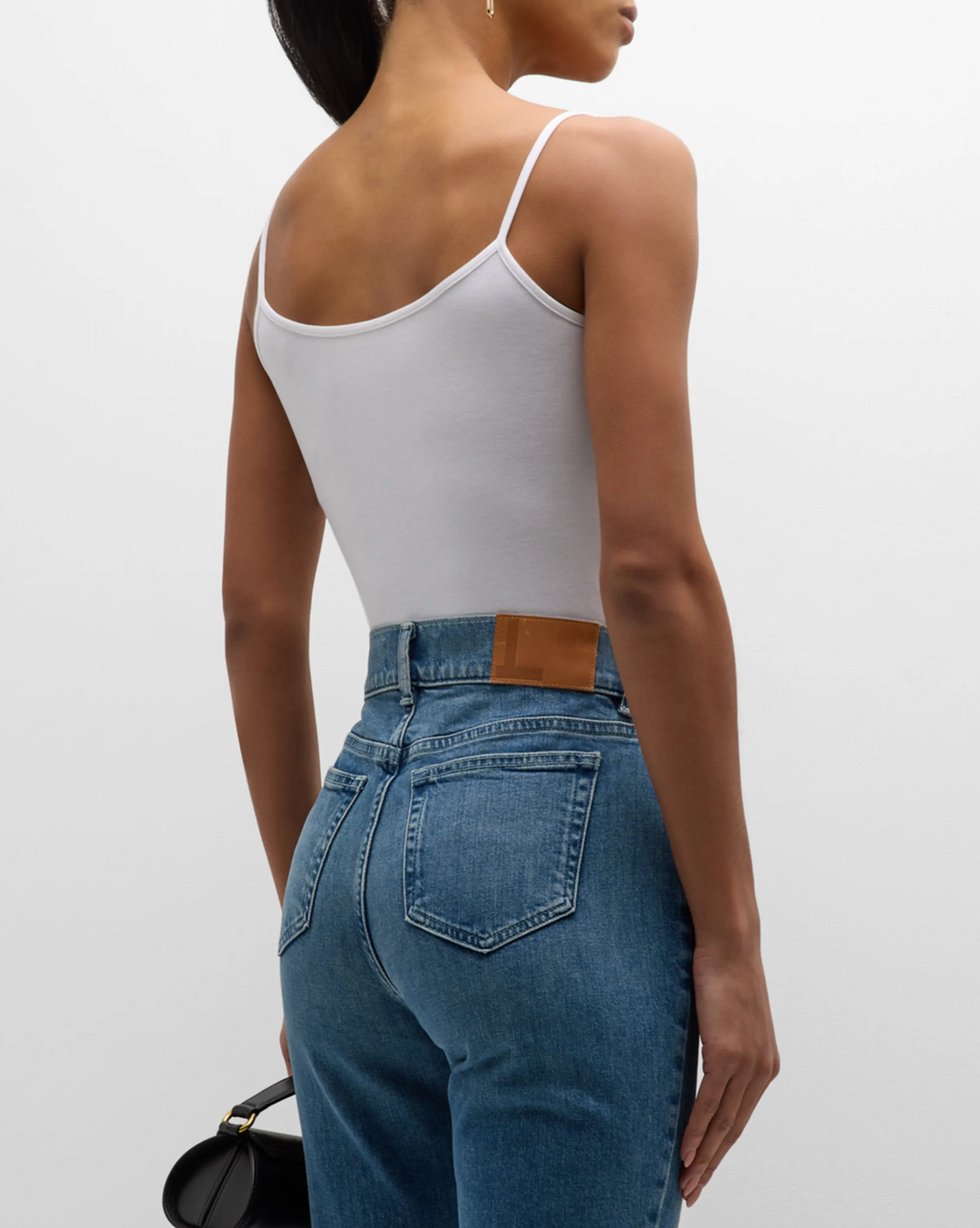Person wearing a white tank top and blue jeans on a plain background