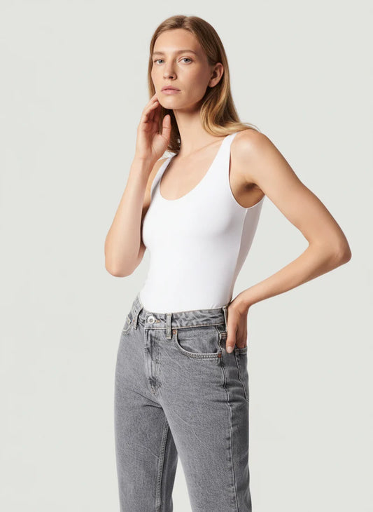 Woman wearing a white tank top and gray jeans against a light background