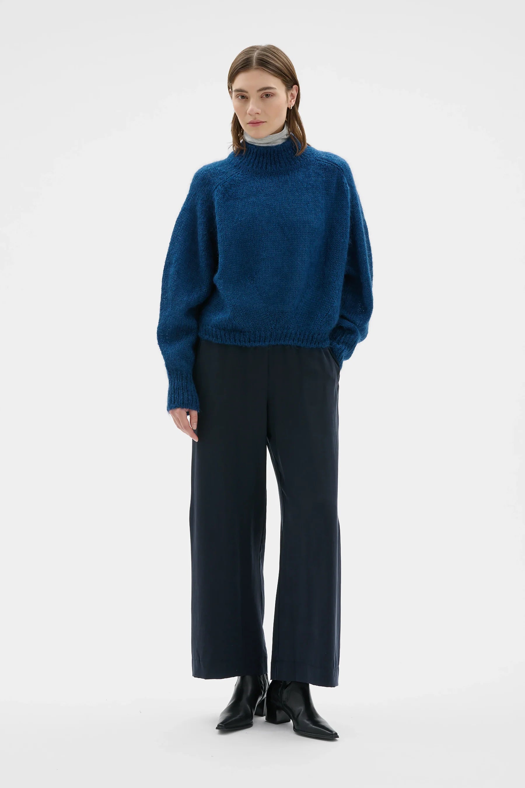 Person wearing a blue sweater and dark pants on a white background