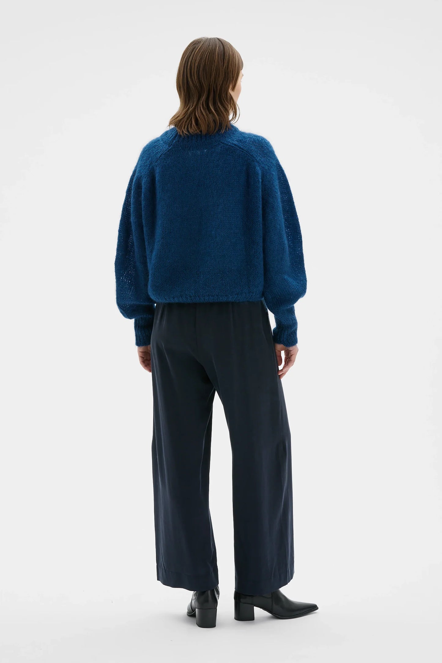 A model shown from the back wearing a textured dark blue cropped sweater and dark navy wide-leg trousers, standing against a plain white studio background.