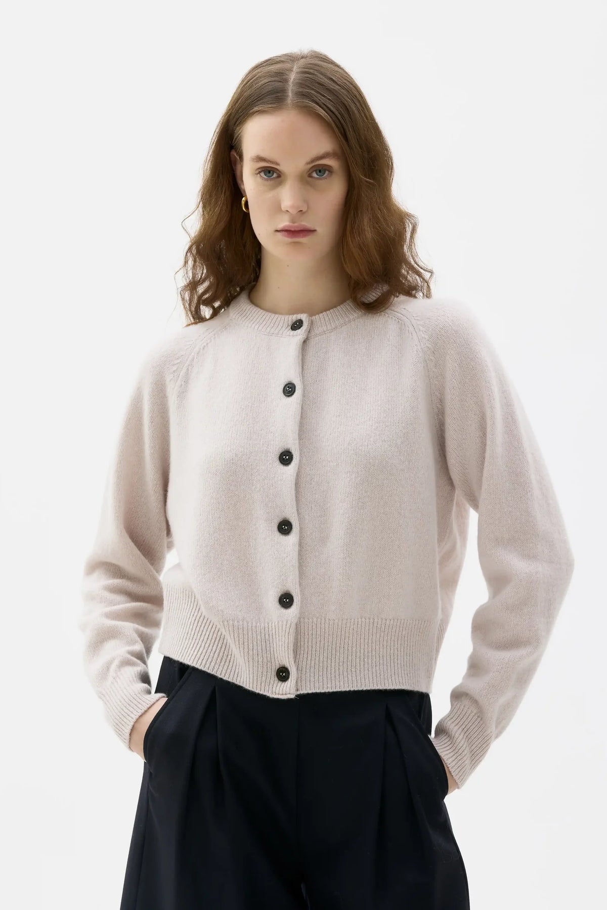 Woman wearing a light beige cardigan with black buttons on a white background