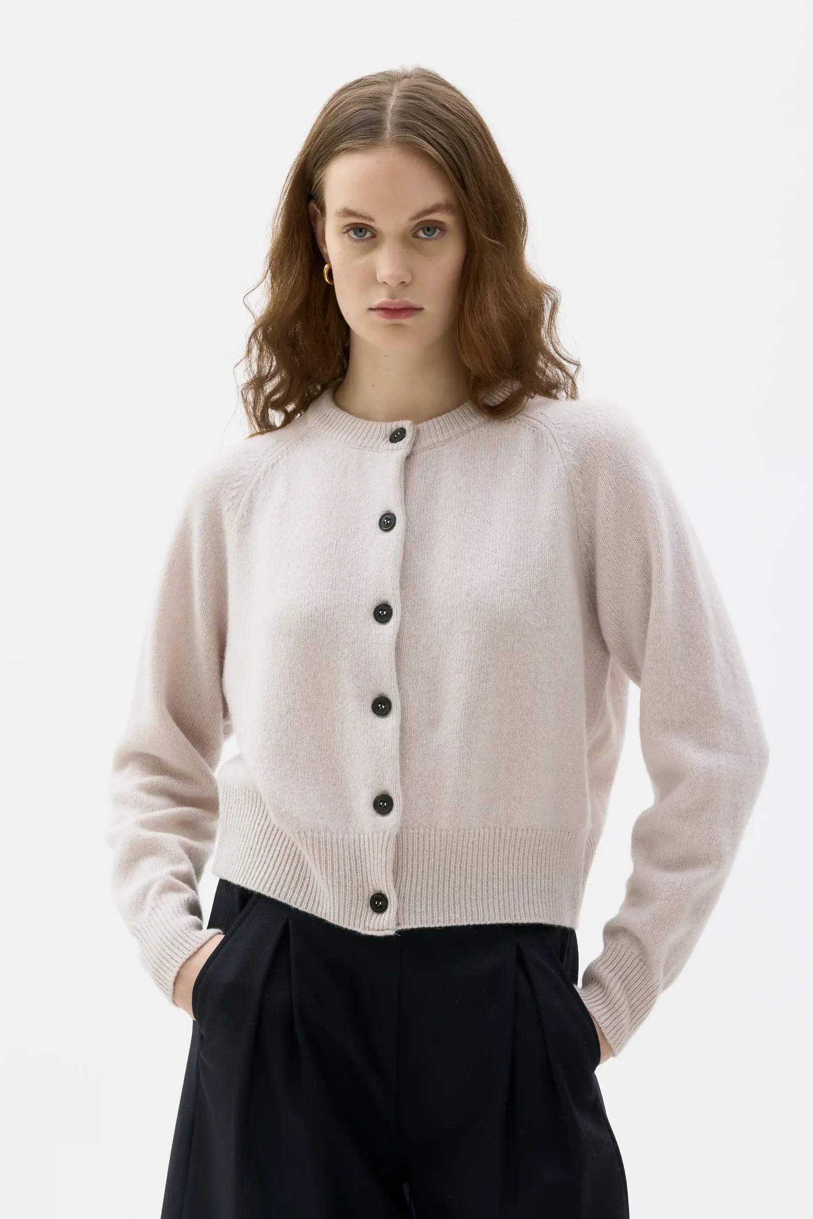 Woman wearing a light beige cardigan with black buttons on a white background