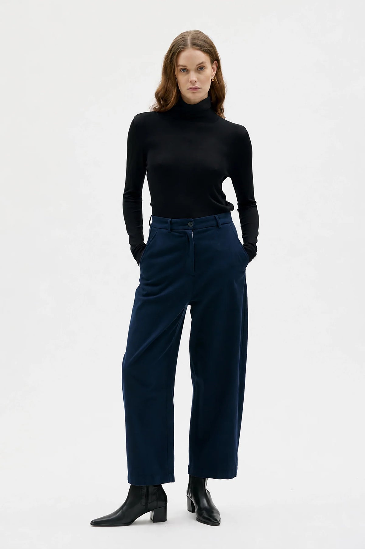 Woman wearing a black turtleneck and navy pants on a white background