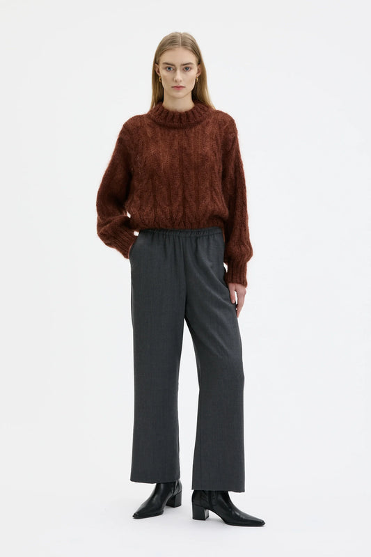 Person wearing a brown sweater and gray pants on a white background