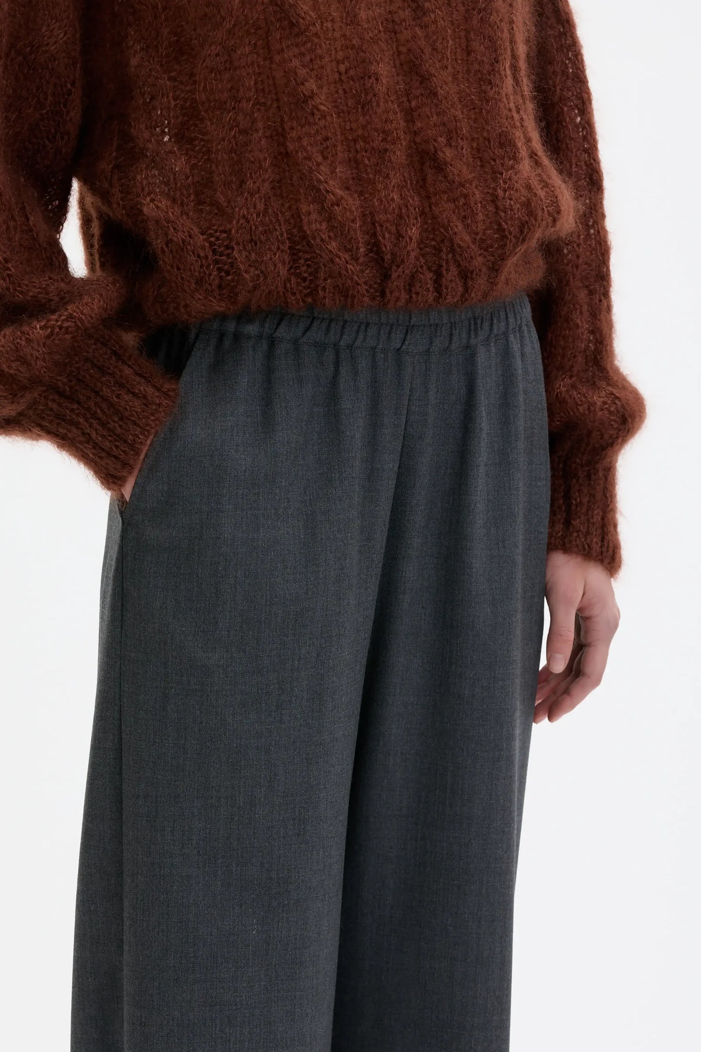 Person wearing a brown sweater and gray pants on a white background