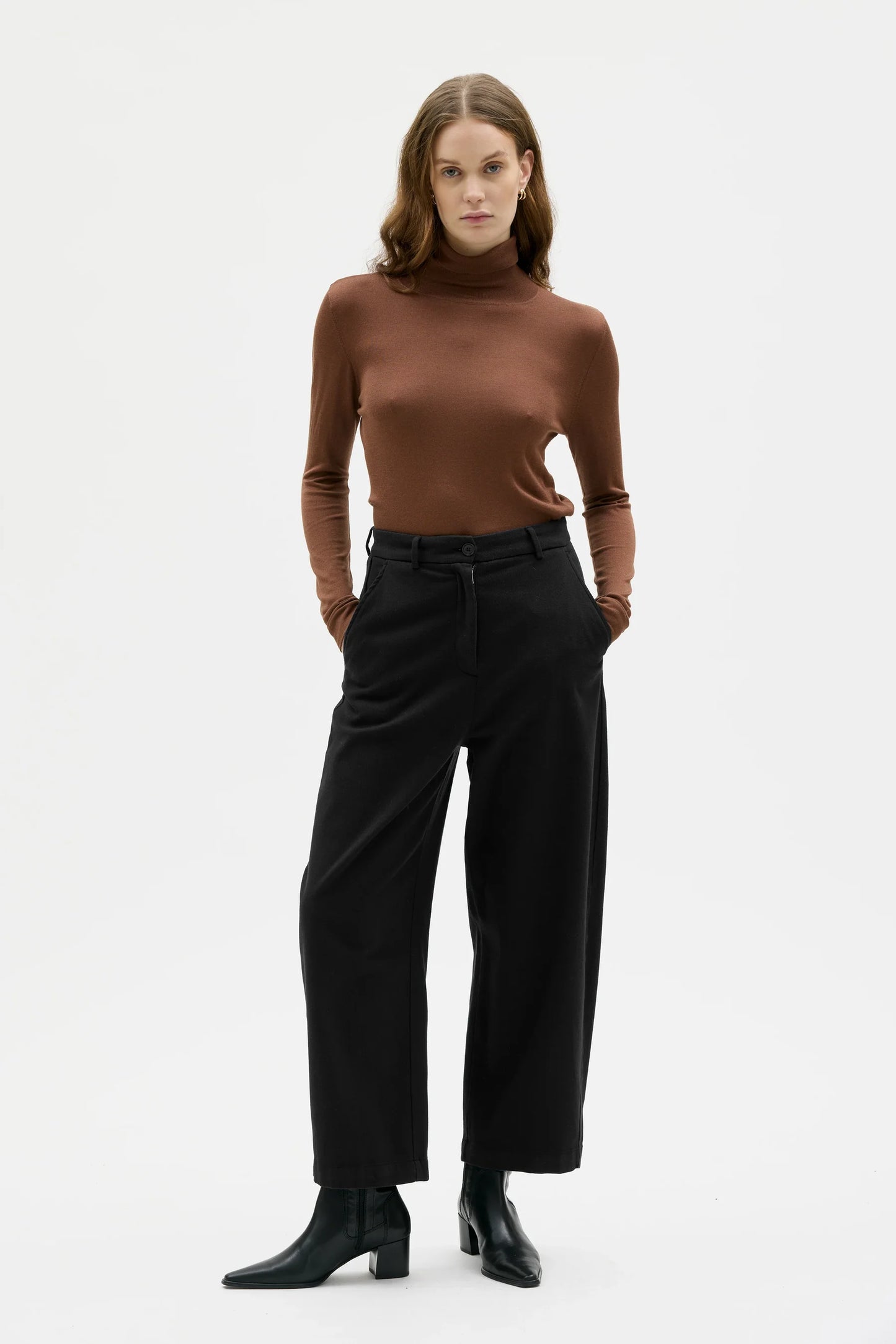 Woman wearing a brown turtleneck and black pants on a white background