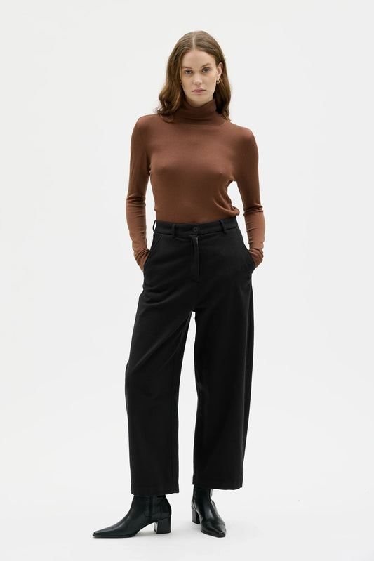 Woman wearing a brown turtleneck and black pants on a white background