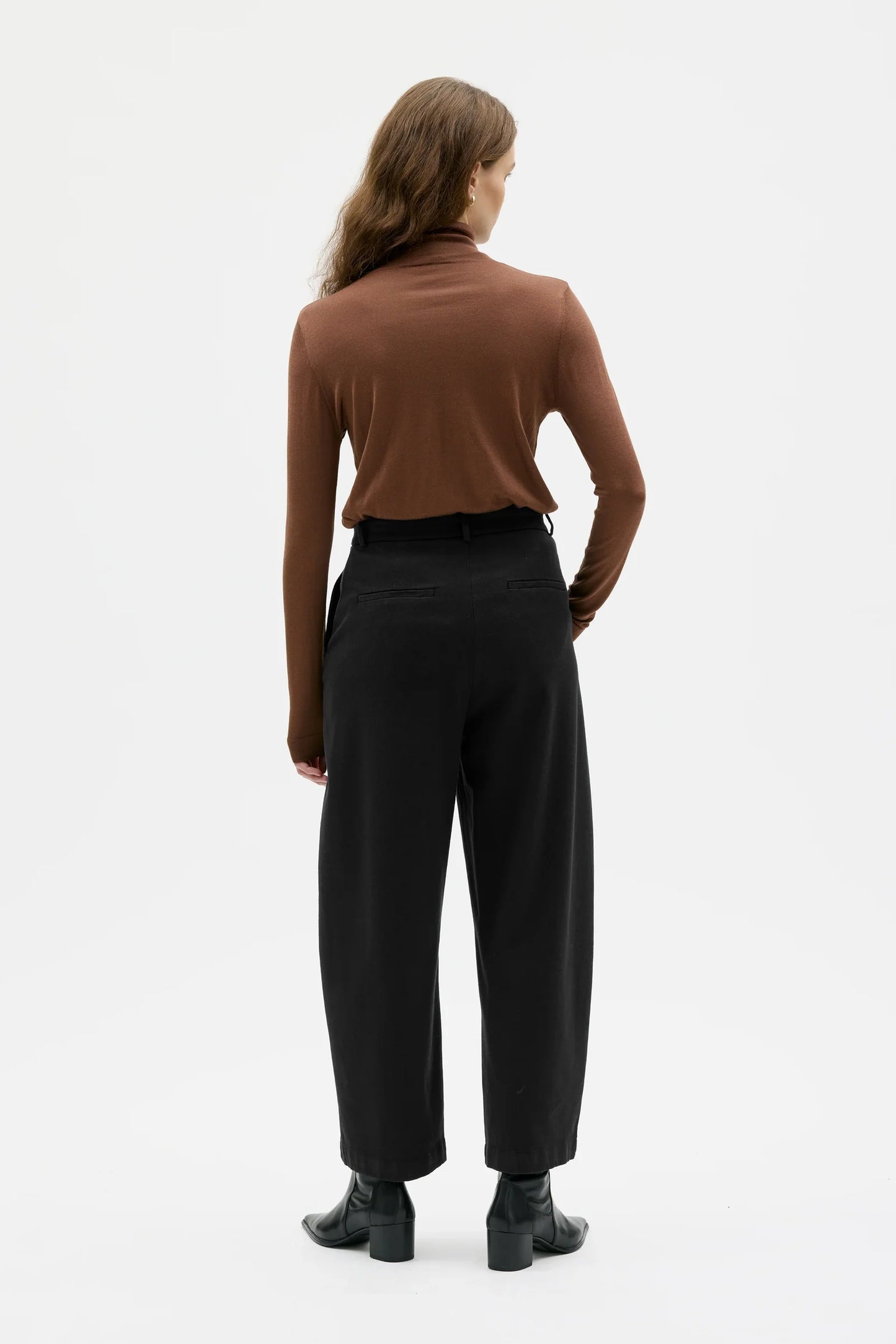 Woman wearing a brown turtleneck and black pants on a white background