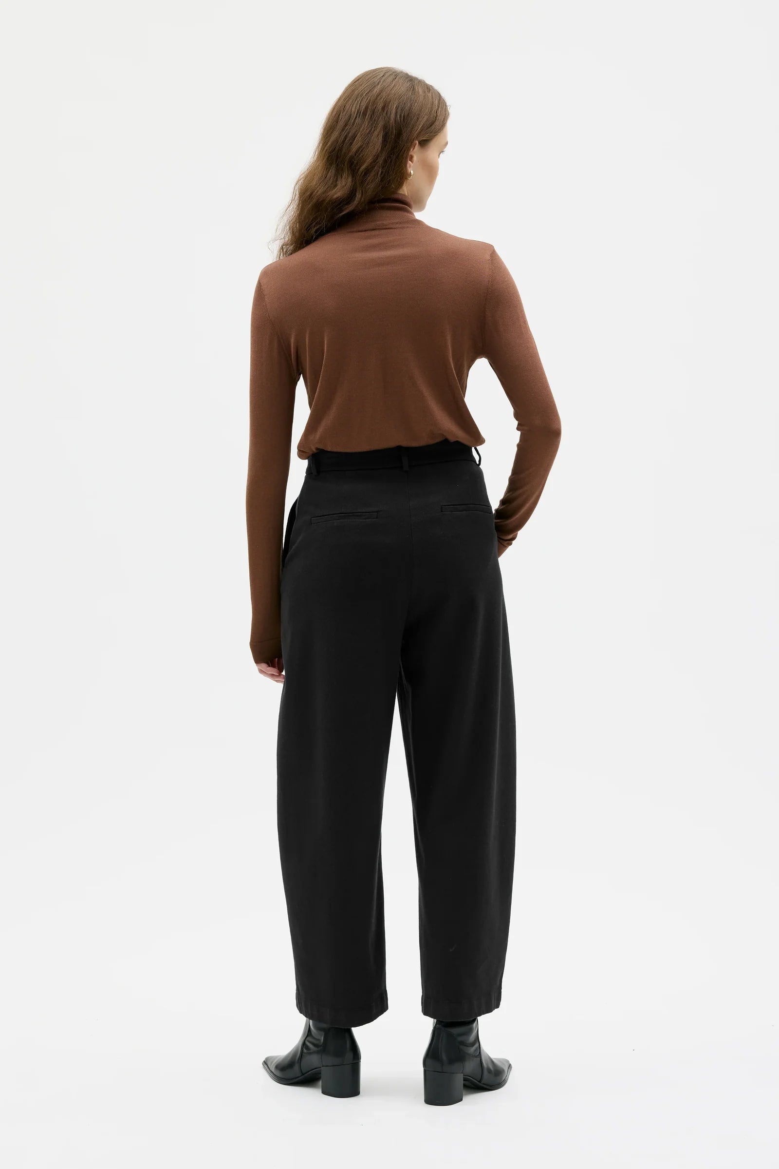 Woman wearing a brown turtleneck and black pants on a white background