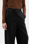 A close-up of a person wearing black wide-leg trousers with a brown long-sleeve top, cropped from the chest down.