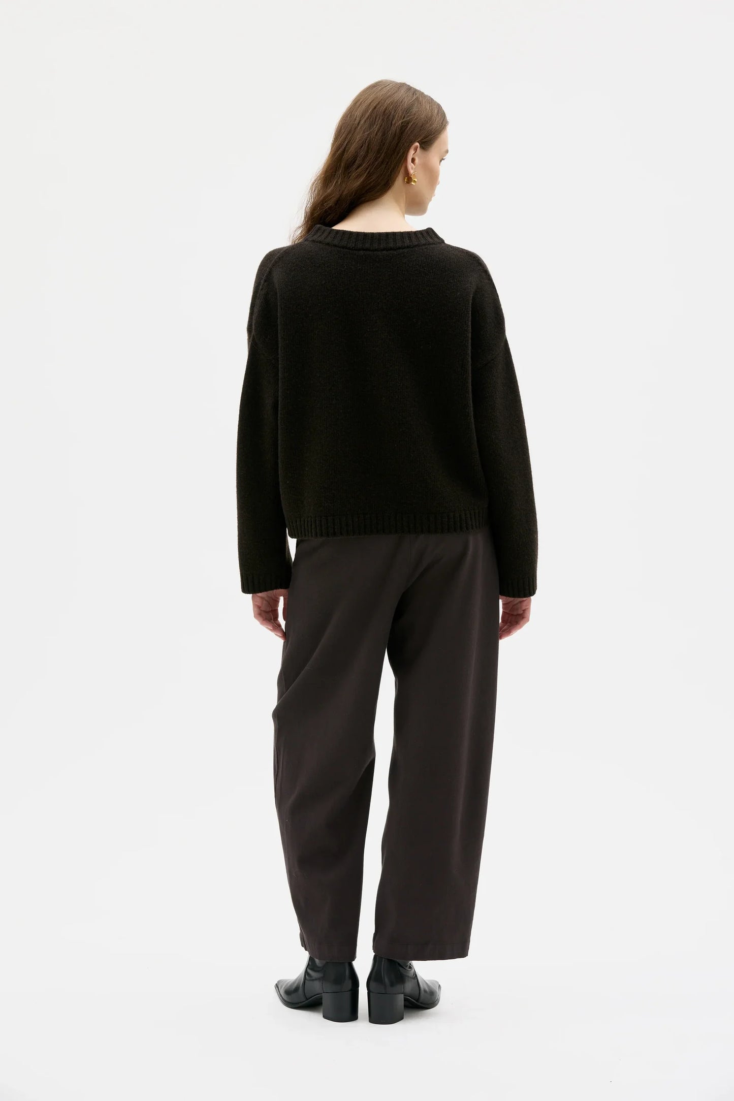 Person wearing a brown cardigan and dark pants on a white background.