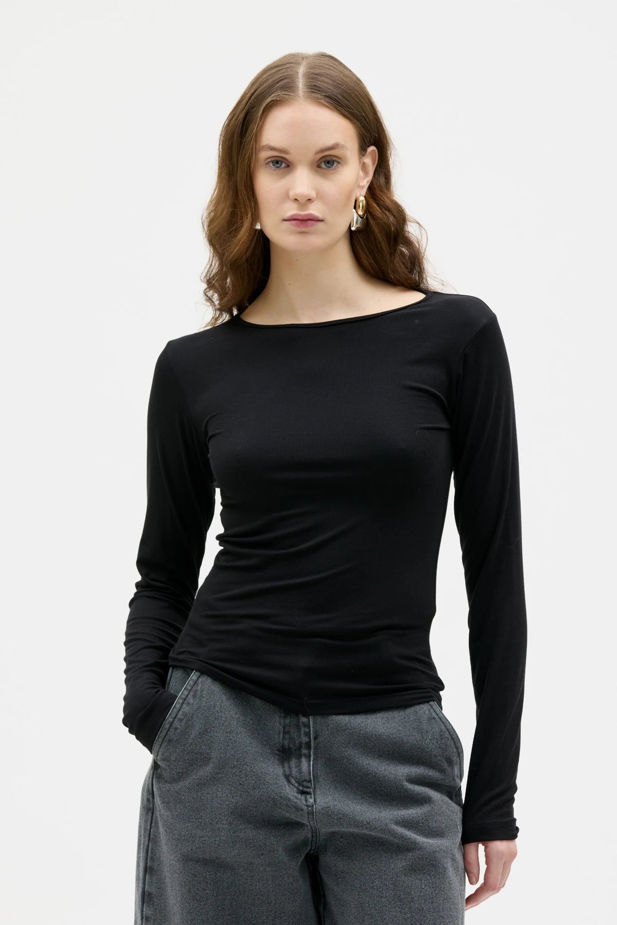 Woman wearing a black long-sleeve top and gray pants on a white background