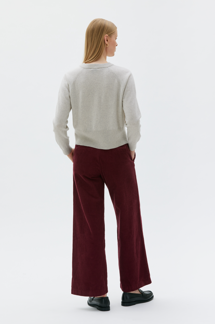 Rear view of Woman wearing sand colored cropped cardigan with burgundy pants.