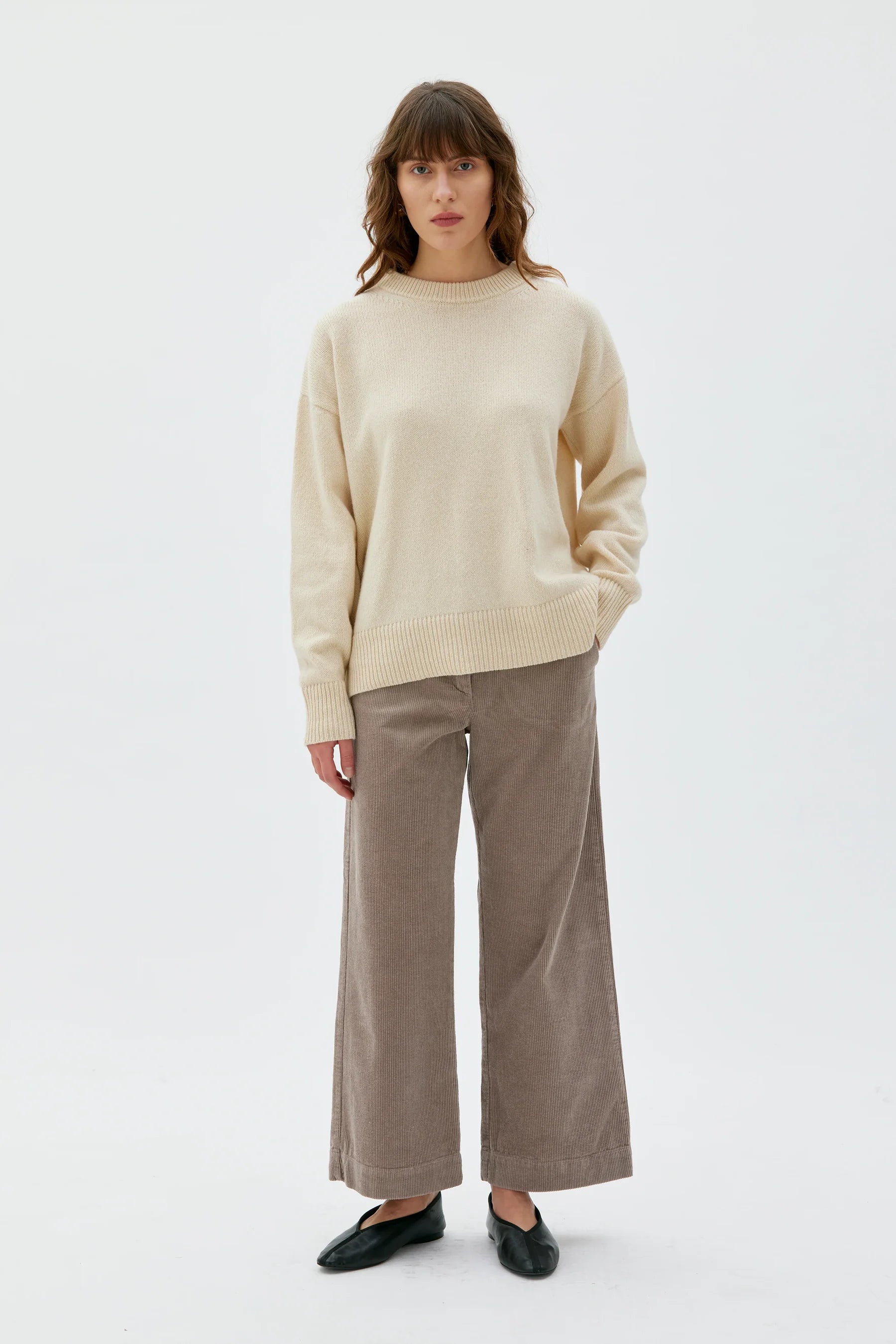 Woman wearing a beige sweater and brown pants on a white background