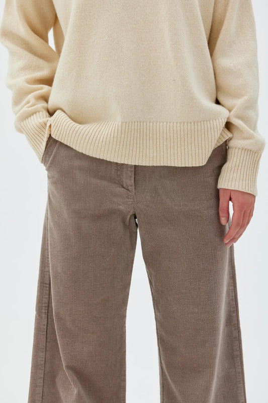Person wearing a beige sweater and brown pants on a white background