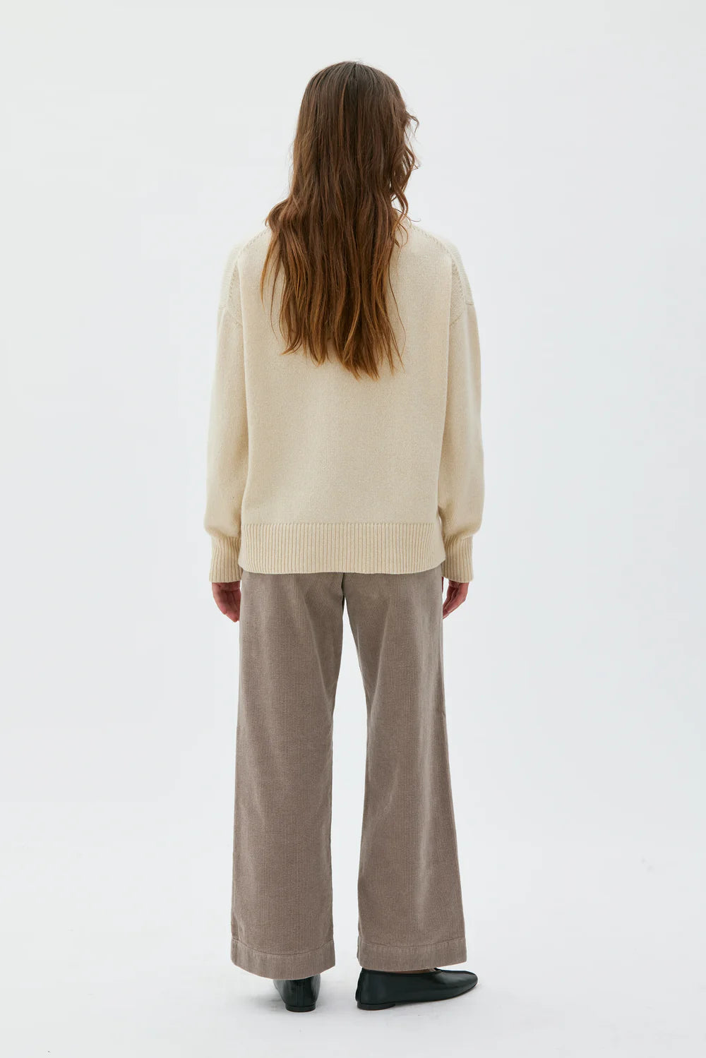 Person wearing a beige sweater and beige pants on a white background