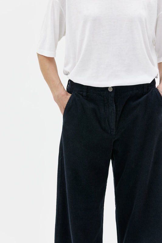 Person wearing a white shirt and dark pants on a plain background