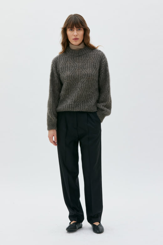 Woman wearing a patterned sweater and black pants on a white background