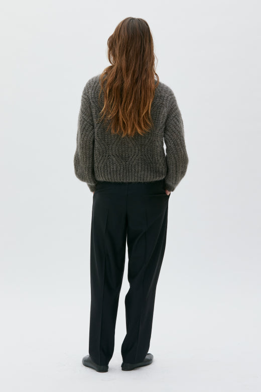 Person wearing a gray knitted sweater and black pants on a white background