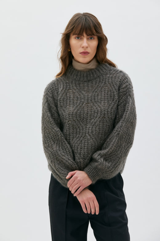 Woman wearing a chunky knit sweater against a plain background