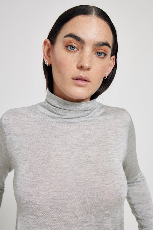 Person wearing a gray turtleneck sweater against a plain background