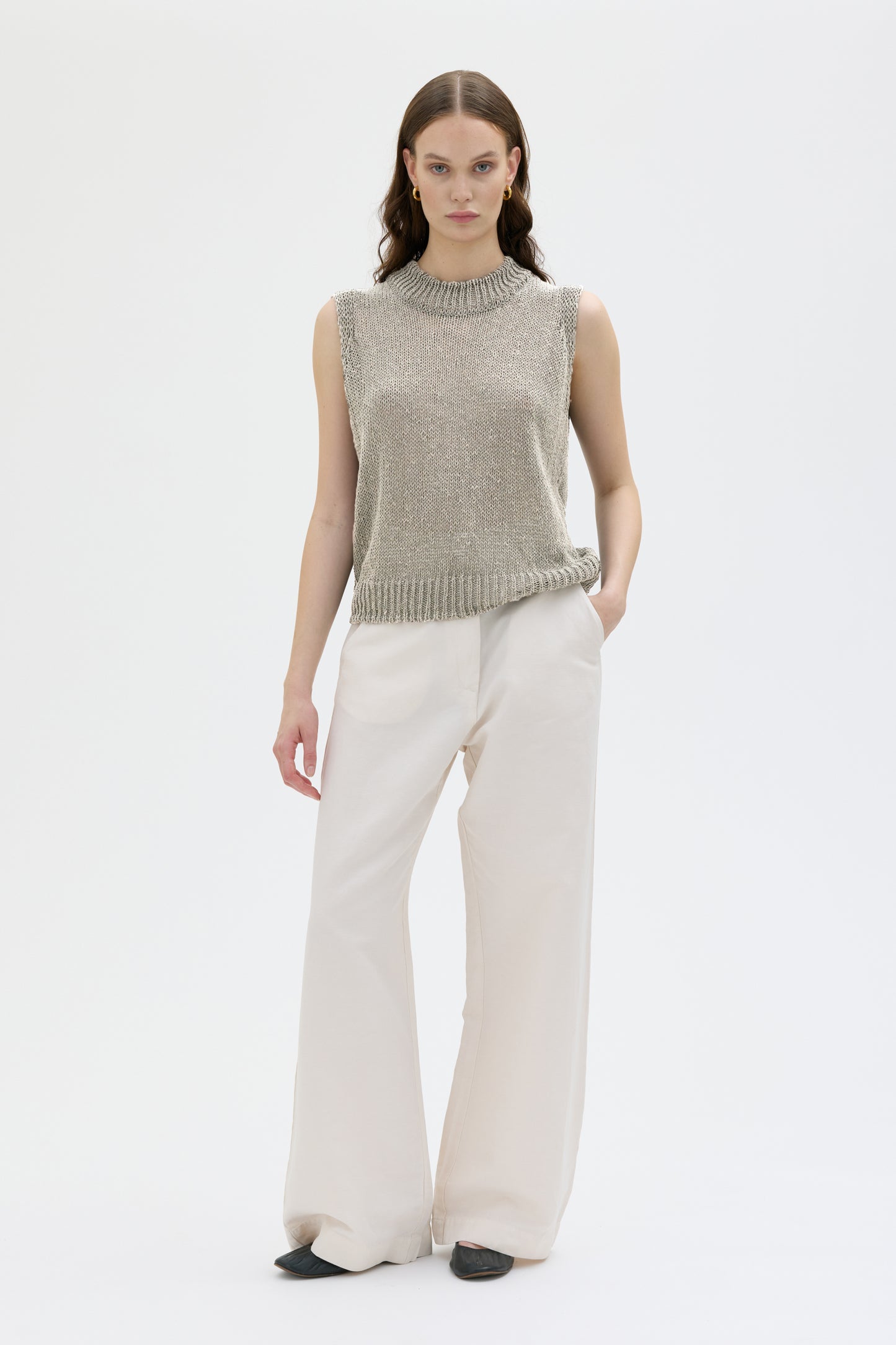 Woman wearing stone color sleeveless top and white pants on white background