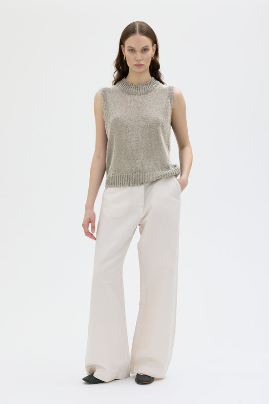 Woman wearing stone color sleeveless top and white pants on white background