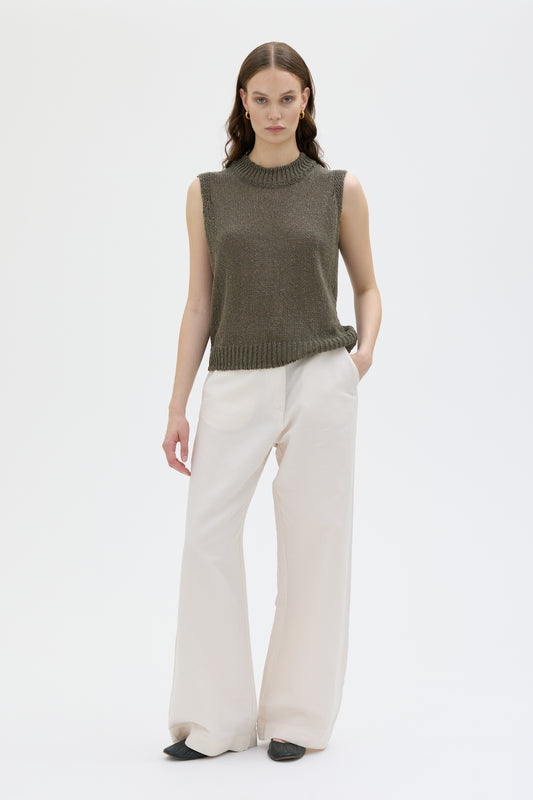 Woman wearing a green sleeveless sweater and white pants on a white background